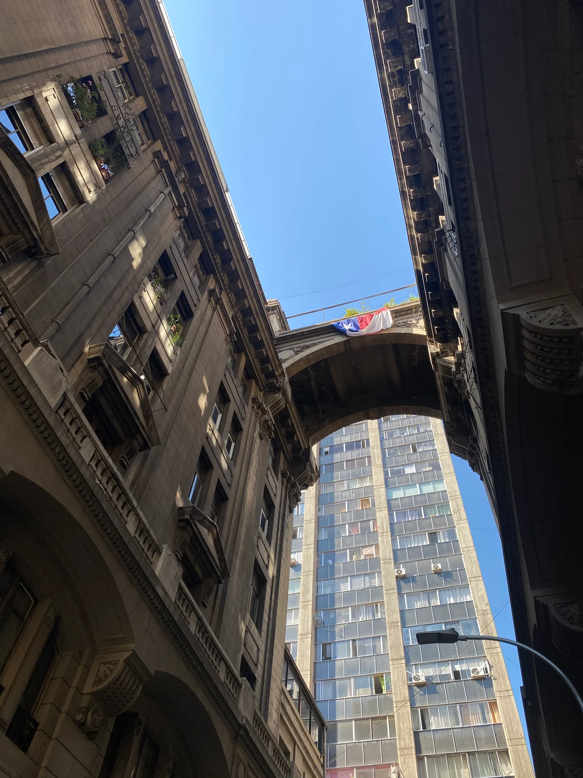 Vista hacia el cielo entre las fachadas y el puente del entorno de Paseo Phillips, Santiago Centro
